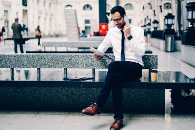 Mutlu erkek yönetmen kitle iletişim araçları yoluyla smartphone uygulama ortakları ile temas sırasında bilgileri kontrol zarif elbise giymiş. Telefonu açık havada konuşurken sahip pozitif girişimci