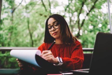 Yetenekli kadın Yöneticisi yapma accountings ve bütçe raporu kontrol numaraları, gözlük yazılı olarak genç iş kadını için yaratıcı başlangıç projesi dizüstü bilgisayar kullanarak uzaktan çalışma planı notlar