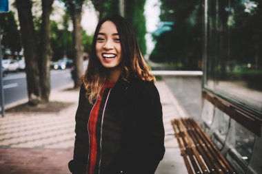 Varoluş üzerinde otobüs durağı, gündelik kıyafeti hafta sonu caddenin üzerinde yürüyen kamera bakarak gülen mutlu hippi kız açık havada duran boş vaktinizi neşeli Asyalı kadın portresi