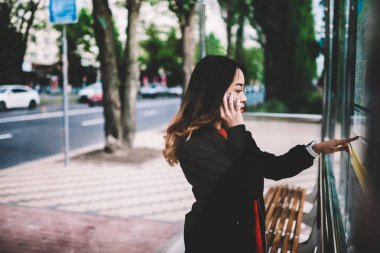 Kadın Seyahat otobüs durağına otobüs durağı cep telefonu iletişim üzerinde duran harita üzerinde daha iyi yol seçme gezici genç kız arkadaşıyla konuşurken toplu taşıma hakkında bilgi okuma