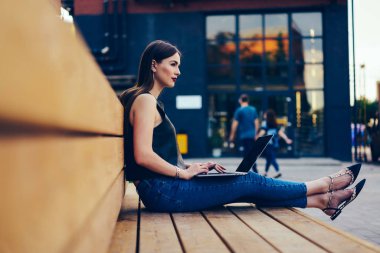 Çekici düşünceli öğrenci rahat kıyafet uzak yolu ile kullanma dizüstü bilgisayarda sunum yaparken bakarak giyinmiş. Açık havada bankta oturan ücretsiz vakit şirin dalgın esmer