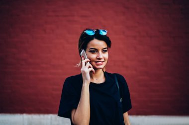 Şirin mutlu kadın kişi alan reklam ile renkli duvar yanındaki yaz yürüyüş sırasında modern telefonla konuşuyor. Pozitif blogger rekreasyon promosyon arka plan yakın kentsel ayarı, zevk