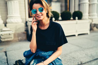 İyi görünümlü şık erkek siyah t-shirt üzerinde cep telefonu konuşurken içinde giyinmiş. Açık havada oturma kentsel ortamda dijital smartphone üzerinden iletişim trendy mavi güneş gözlüğü neşeli genç kadın