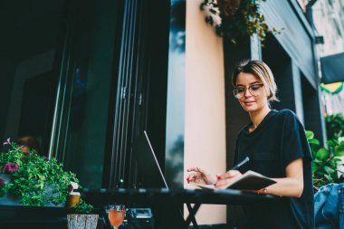 Genel kavramlar dışında oturan yeni başlangıç projesi için aşağı yazma gözlük genç güzel kadın girişimci. Dizüstü bilgisayar ve not defteri kentsel ayarı çalışma güzel hippi kız