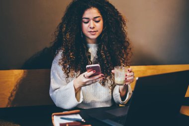 Genç çekici hippi kız haber paylaşımı ve sosyal ağ üzerinden cep takipçileri ile sohbet trendy giyim giymiş. Kafede oturan ve online ödeme yapmadan yetenekli yazarı