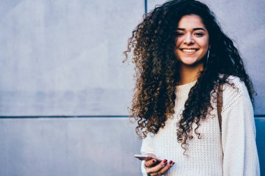 Yarım uzunluk portre sevimli gülümseyen öğrencinin kentsel ayarda ve alışveriş online yolu ile telefon ve 4 g gezinme Internet. Yaz dışında yürüyüş yaparken kameraya seyir tatlı hippi kız