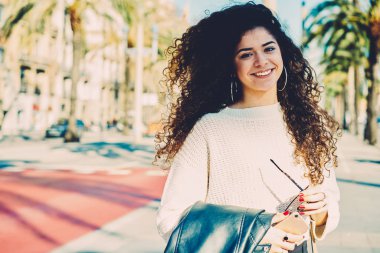 Yarım uzunlukta güneşli yaz gününde şehir etrafında geziniyor güzel kıvırcık saçlı genç gülümseyen kadın portresi. Bahar sokak rekreasyon tadını çıkarırken kameraya bakarak şirin mutlu genç