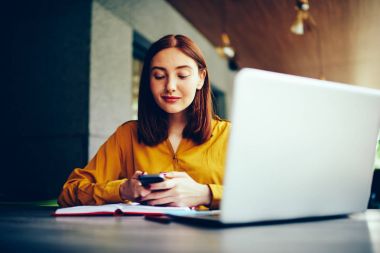 Bildirim smartphone cep telefonu ile kontrol Burun piercing ile genç çekici kadın grafik tasarımcı kablosuz internet'e bağlı. Yetenekli büyüleyici freelancer ileti gönderme sırasında mesafe işe
