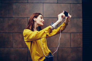 Şık Kızıl saçlı hippi kız selfie smartphone yapma ve sosyal ağ profili resimde duvar reklam alanı için kısa mesaj ile yanındaki yürüyüş sırasında güncelleştirme sırasında kamera için poz