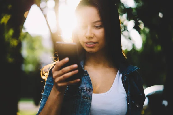 美しい女性ブロガーが太陽の下で屋外で立って現代の携帯電話の高速 接続を使用してインターネットのウェブサイトに新しい記事を Publicating します 若い女性の携帯電話に Sms メッセージを送信します — ストック写真