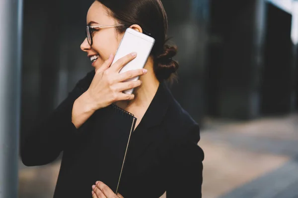 眼鏡の手でフォルダーを押しながらよそ見しながら携帯電話で同僚とのコミュニケーション豊かな女性銀行のイメージをトリミングします スマート フォンで話している成功した実業家 — ストック写真