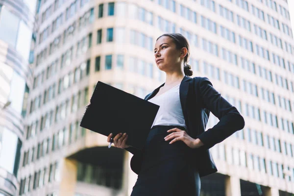 自信的女商人身着正式服装持有黑色文件夹在手与模拟区域 并期待直站在街道上办公大楼促销背景为您的金融新闻 — 图库照片