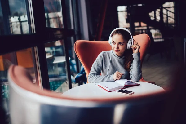 Pensive female student enjoying music in modern headphones.