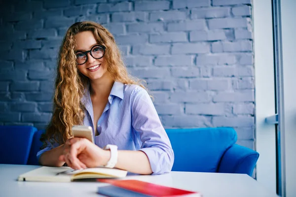 Estudiante Positivo Con Pelo Rizado Sosteniendo Teléfono Moderno Mano Sentado —  Fotos de Stock