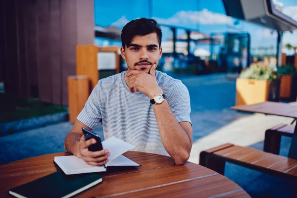 Hipster guy waiting for online booking confirmation in web store holding phone.