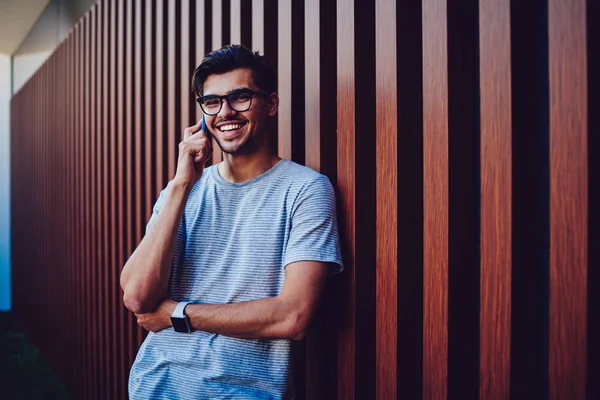 Cheerful young man in eyeglasses laugh during phone conversation.