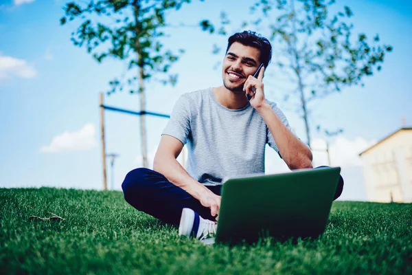 Evet yeşil çim üzerinde modern netbook ile oturan neşeli genç adam portresi.