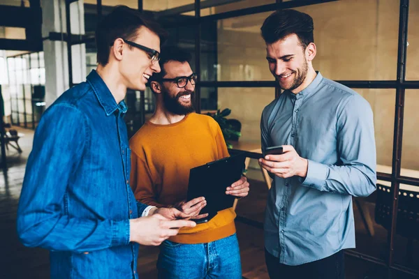 Neşeli takım üyeleri smartphone cep telefonu ile video izlerken ve şaka tatilinde eğleniyor.