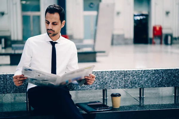 Handsome smart bankir dressed in stylish formal wear reading columns with financial news.