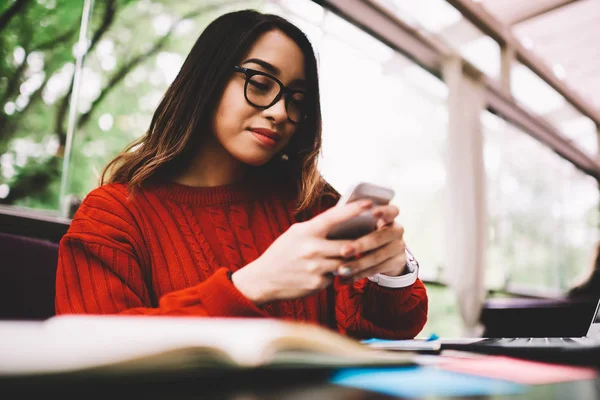 Smiling young female reading notification from banking service making payment in application on mobile, hipster girl chatting in social networks with friend satisfied with internet connection