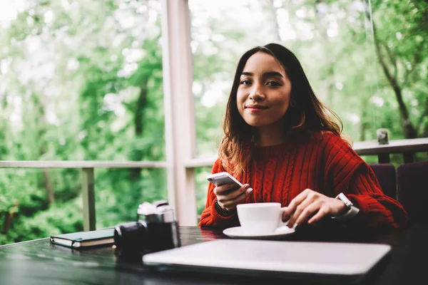 Portrait of young asian woman looking at camera while updating application on smartphone in cafe, hipster girl enjoying coffee break blogging in social networks sharing photos with followers on mobile