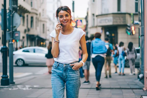 时尚开朗的年轻女子身着白色 T恤与模拟区的文字信息漫步在现代城市的街道上 并与朋友在电话上交谈 多彩的促销背景 — 图库照片