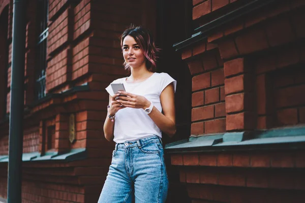 大学の近く屋外で立って現代の電話のメールをチェック カジュアルな服装でスタイリッシュな学生 ストレートを見ながらスマート フォン デバイスのオンライン支払いを作る魅力的な若い女性 — ストック写真