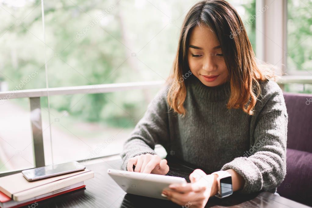 Young female student resting in cafe terrace watching videos on portable pc, hipster girl browsing website of online banking service for making money transaction easy and fast during coffee break