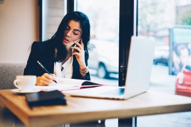 Yeni görev için not defteri kayıt ve müşteri yolu ile kullanma smartphone cep telefonu ile iletişim çekici dalgın grafik tasarımcı. Genç sevimli kadın bankacılık sorunu çözmek için çevrimiçi destek söz