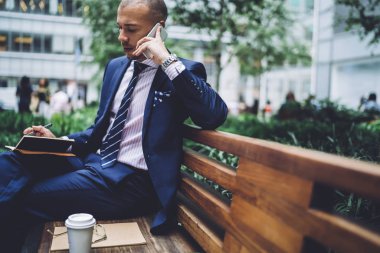 Düşünceli erkek avukat telefon konuşmayı icra müdürü ile hizmet operato bankacılık mobil danışmanlık sırasında konuşurken bilgi yazma bankta oturmuş ayrıntıları belirterek çalışma hakkında
