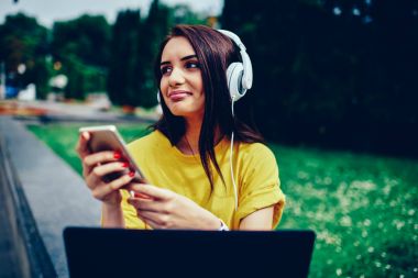 Kulaklıklar ve uygulama Smartphone üzerinden radyo dinlerken zevk mutlu çekici kadın blogger bağlı 4 g için Internet. Boş vakit dışında modern cihazlar ile pozitif sevimli esmer