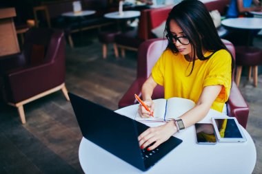 Genç esmer öğrenci ders projesi için internet'e bağlı dizüstü bilgisayar Web sayfalarında yararlı bilgiler arama durulması. Uzaktan kafeteryada çalışan dalgın grafik tasarımcı