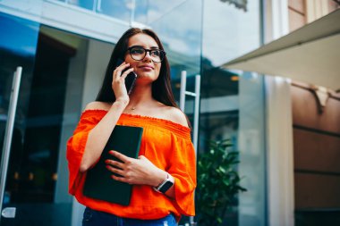 Dalgın kız öğrenci çekici trendy giyim kentsel ayarı serbest zaman sırasında modern telefonla konuşurken giymiş. Havalı gözlükler modern aygıt yolu ile irtibata olumlu genç hippi kız