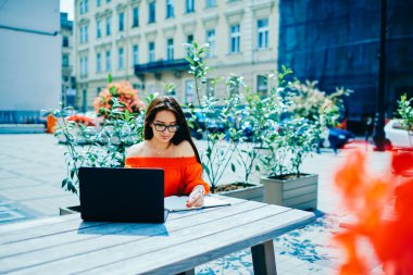 Şık gözlük planlama uygulama için 4 g bağlı dizüstü kullanarak çalışma süreci dalgın çekici grafik tasarımcı. Büyüleyici yetenekli esmer freelancer bilgileri Defteri'ne yazma