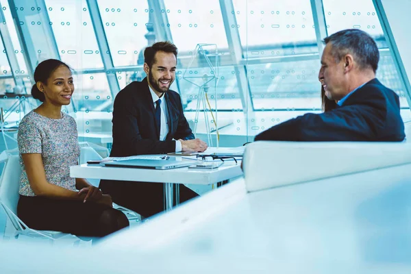 Diversity group of professional employees having meeting with proud CEO communicating in friendly atmosphere, smiling crew of architects discussing working process with investors at meeting table