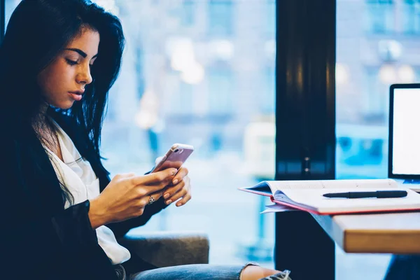 Cropped image of cute hipster girl checking notification on cellphone during chatting with followers in social networks.Young pondering businesswoman sending message via email to partner in cafe