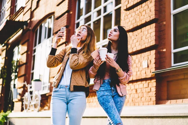 Female best friends in casual outfit shooting video of smartphone fascinated with city buildings,hipster girls taking picture of urban settings for blogging in networks walking with coffee to go