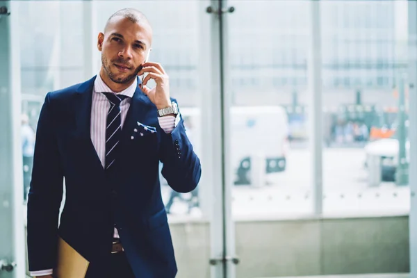 Serious banker having mobile conversation about work with colleague standing near publicity area,self-confident executive manager in formalwear discussing business plans during phone conversatio