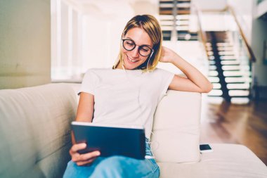 Mutlu erkek Eyewear komedi Divan modern iç dairede neşeli hippi kız kanepede tembel eğlence komik videolar zevk memnun dinlendirici dinleniyor taşınabilir PC'de izlemek