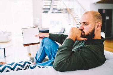 Düşünceli erkek roman, dalgın hipster adam rahat ev atmosferinin dinlenme hobi ile boş zaman zevk edebiyat düşkün okuma bitirme kitabın içeriği analiz rahat kanepe oturma