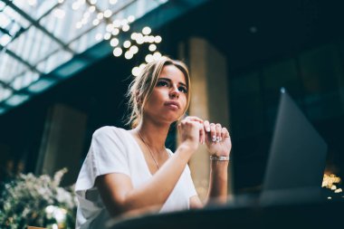 Düşünceli çekici sarışın kadın uzak modern dizüstü bilgisayarda kafede otururken seyir görünüm altında. Dijital netbook kullanarak yeni fikirler üzerinde düşünme çekici metin yazarı durulması