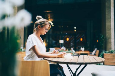 İş ortaklarına tahta masada oturan modern cep telefonuna sms mesaj gönderme gözlük dalgın kadın. Genç kadın kafe mesafe iş sırasında cep haber okuma konsantre