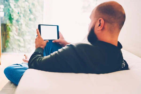 在舒适的沙发上休息的人的看法和观看电影在线 便携式 与模拟屏幕 胡子的家伙花时间在家阅读电子书籍下载在数码片上 — 图库照片