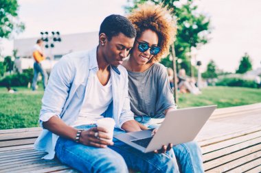 Genç olumlu afro Amerikan çift açık havada eğlence ve Web sitesinde 4 g için bağlı dizüstü komik videoları izlerken trendy kıyafeti giymiş. Mutlu bir adam ve kadın dışında becerikli alet ile dinlenme