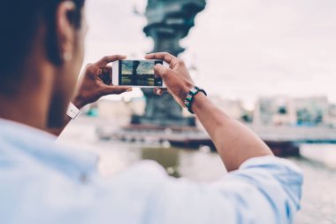 Seçici odak modern cep telefonu tutarak ve showplace Nehri yakınında iyi resim yapmaya çalışan adamın ellerinde. Açık havada gezinme sırasında cep üzerinde fotoğraf yapma turist arkadan görünüm Resim kırpılmış