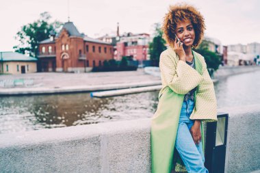 Kentsel ayarı boş zaman zaman harcama ile sokulgan yolu ile hücresel iletişim muhteşem gülümseyen afro Amerikalı kadın. Rekreasyon açık havada sırasında telefonda konuşurken zevk çekici kadın turist