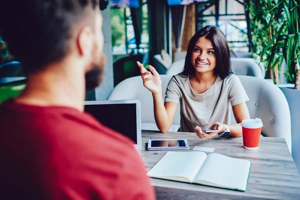 Cheerful female student enjoying collaboration process on common project discussing ideas together using technology, male and female colleagues having friendly  conversation about work in coffee shop