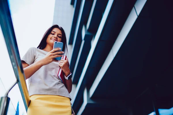 魅力的なブルネットの女性学生の大学 レジャー都市設定の上に立って楽しむスマート フォン更新プロファイルに肯定的な流行に敏感な女の子ブログで休憩中にソーシャル ネットワークに写真を送信します — ストック写真