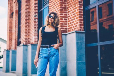 Şık Eyewear Kentsel Yapı açık havada buluştuğun için bekleyen yakınındaki poz ciddi kadın turist, genç ve güzel kadın casual giyim serbest zaman sırasında caddenin üzerinde duran modaya uygun kot pantolon giymiş