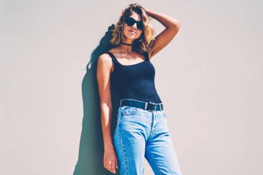 Promosyon arka plan üzerinde zevk eğlence, muhteşem hippi kız açık havada kameraya bakarak saç dokunmadan ayakta modaya uygun kot pantolon poz şık rahat kıyafet güzel kadın beyaz modeli